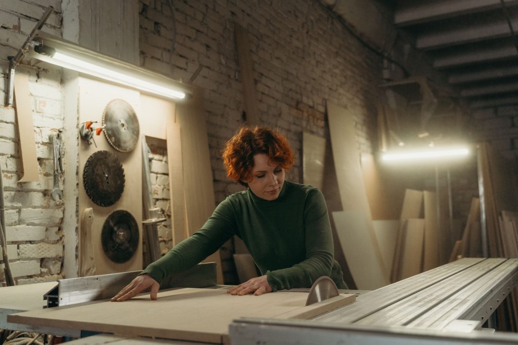A female woodworker carefully guiding a timber panel through a professional table saw in a joinery workshop, bringing precise joinery drafting services to life.