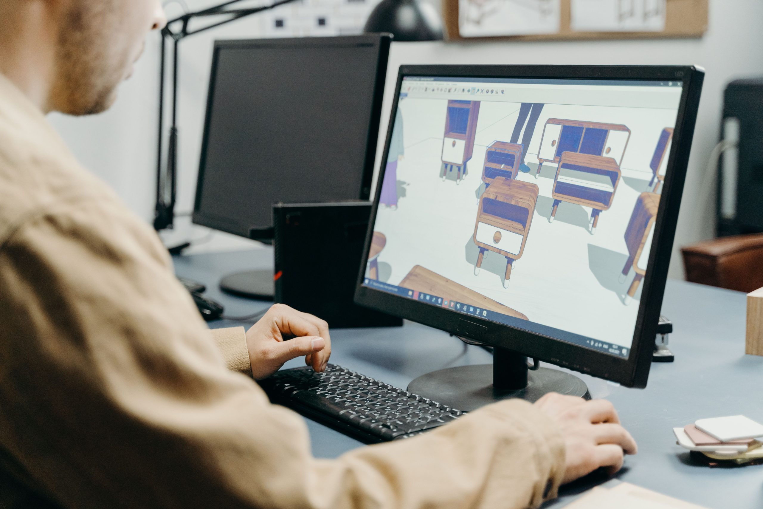 An operator designing custom wooden furniture and cabinetry layouts on a desktop monitor using PYTHA 3D CAD modeling software.