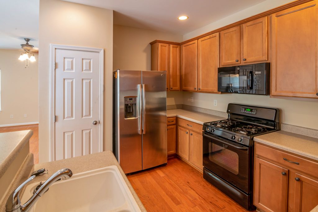 Classic residential kitchen interior featuring light brown timber cabinetry, a stainless steel refrigerator, and a black gas range cooker setup.