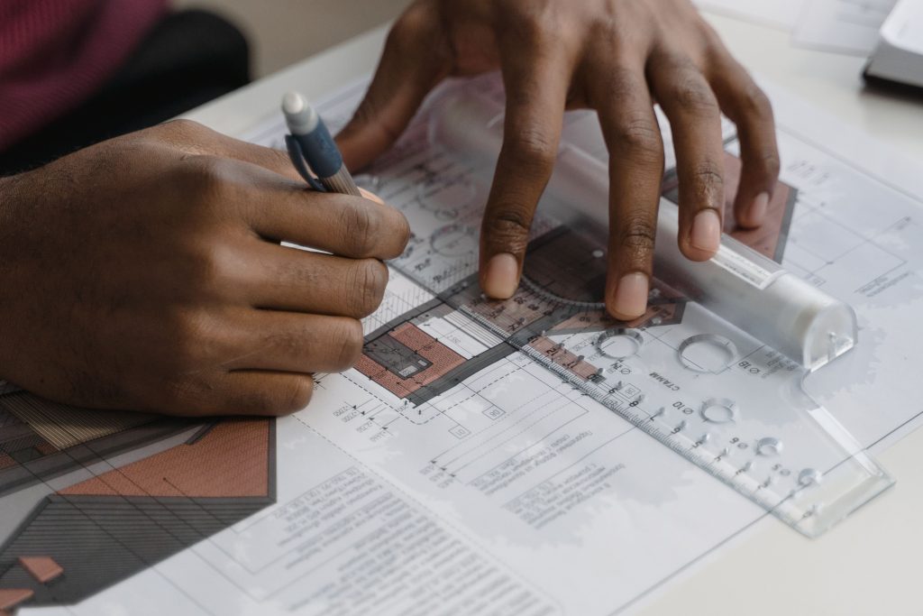 Close-up of a designer using a pen and a plastic technical ruler to draft precise engineering blueprints and production-ready shop drawings.