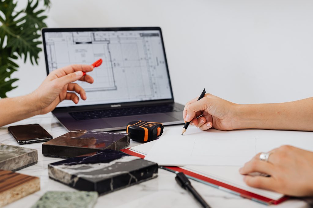 Interior designer sketching plans and reviewing architectural blueprints on a laptop screen to prevent joinery design mistakes.