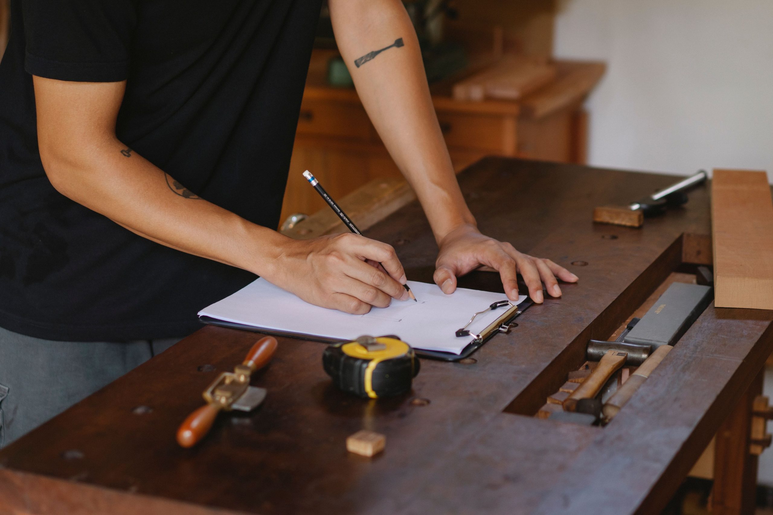 Woodworker drafting specifications on a clipboard at a workbench during the initial phase of the joinery design process.