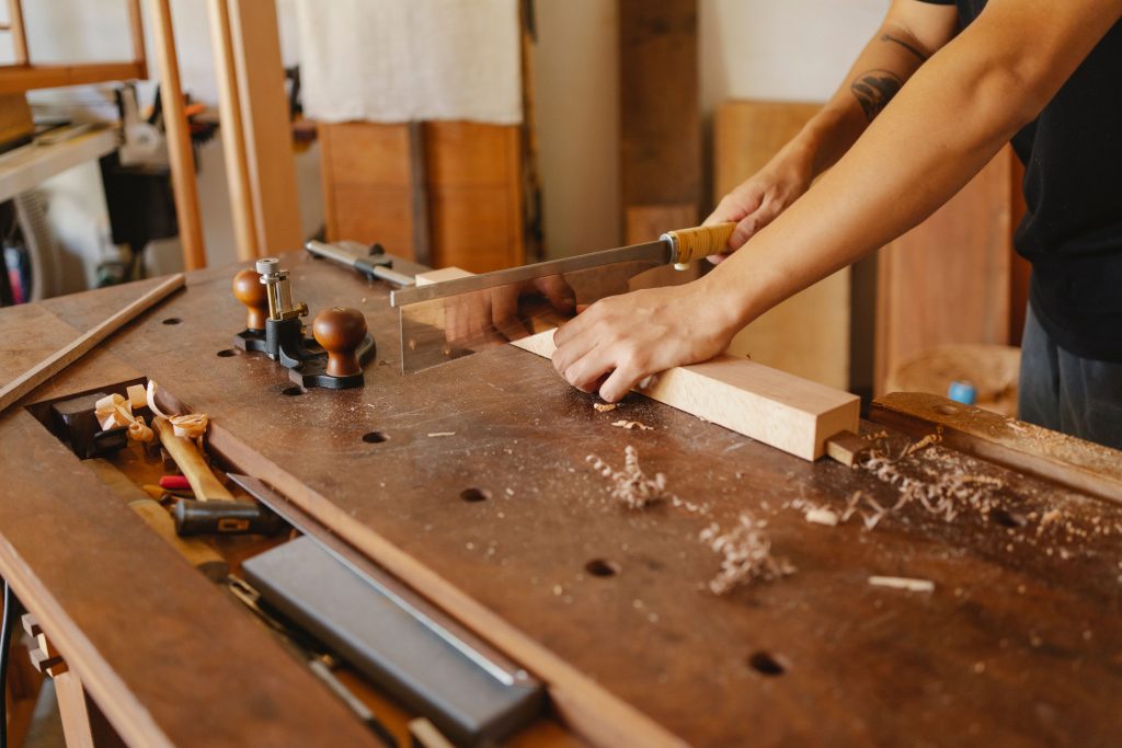 Craftsman cutting timber at a woodworking bench using precise plans from outsourced joinery drafting.
