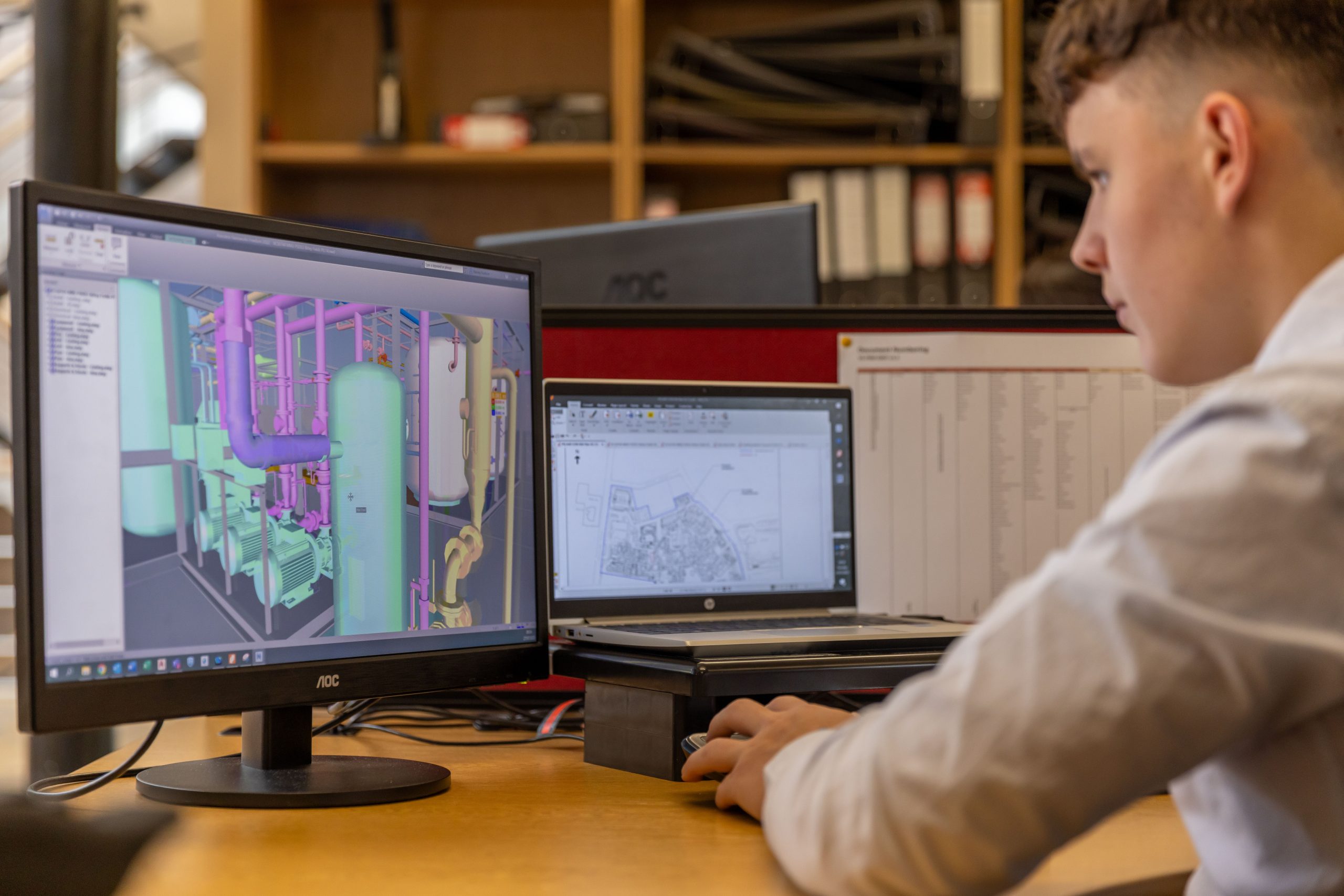 CAD operator analyzing a complex 3D technical model on a dual-monitor workstation, comparing PYTHA vs CAD software performance for industrial design.