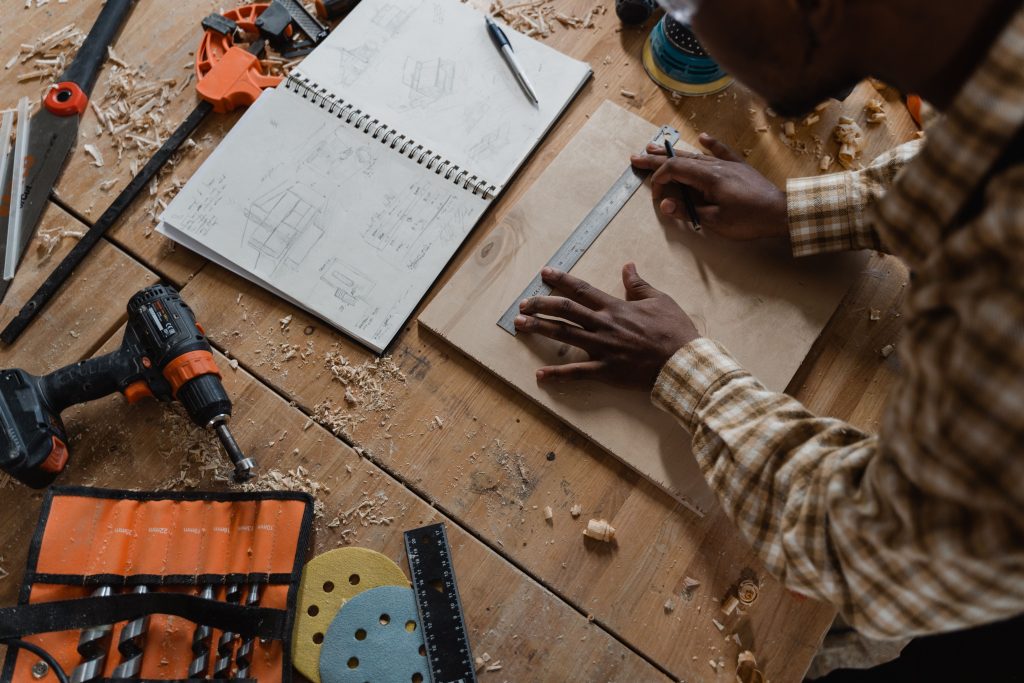 Woodworker measuring timber panel against technical drawings to execute a precision PYTHA manufacturing workflow.